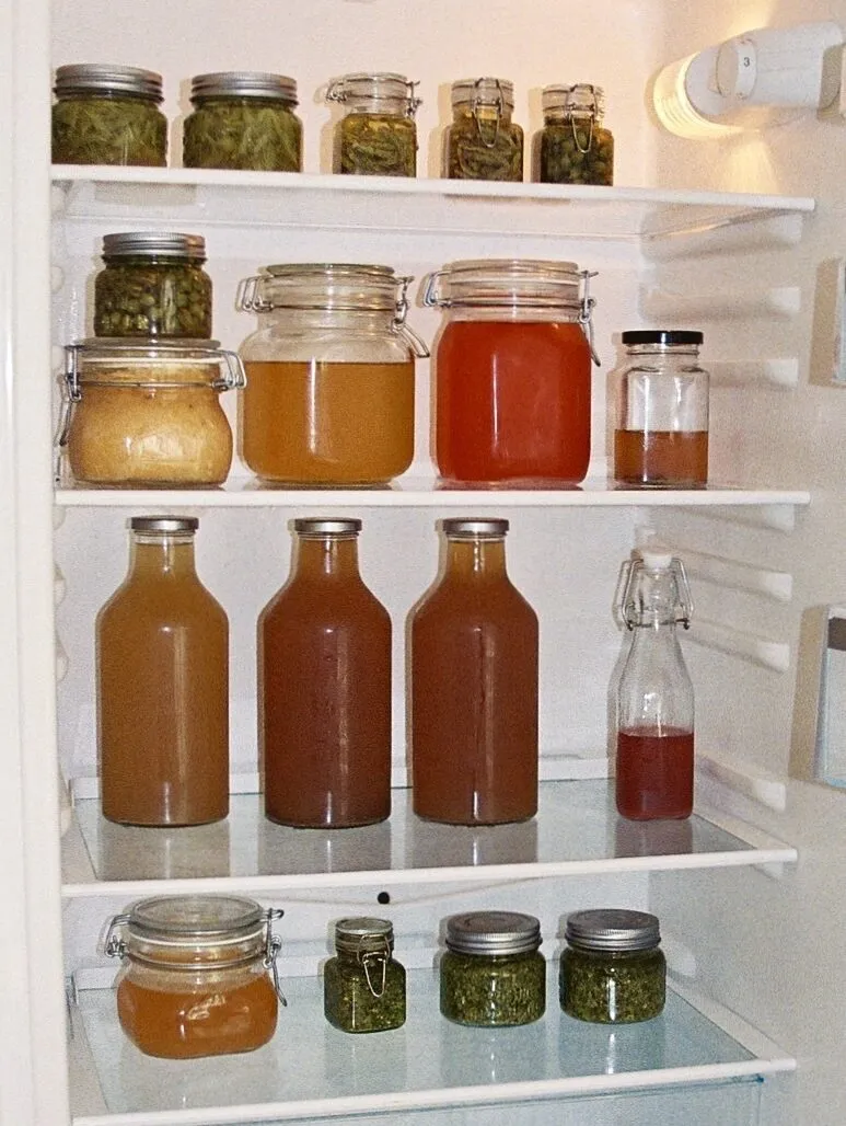 A refrigerator filled with glasses and bottles containing pastes and beverages in various colors.
