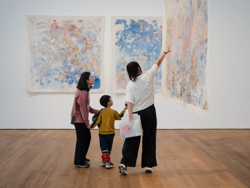 An adult and child visit an exhibition of suspended paintings at Mudam with a museum mediator.