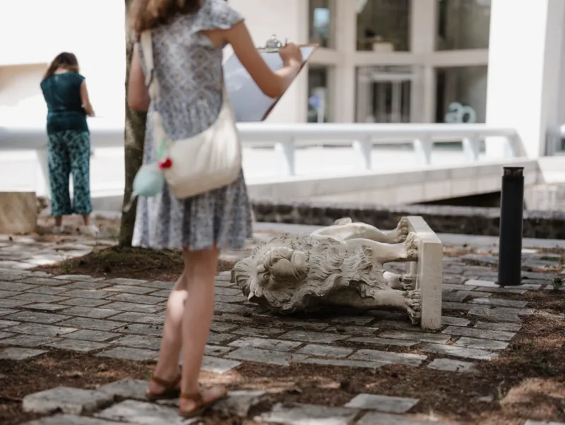 Une jeune fille dessinant une statue de lion renversée devant le Mudam.