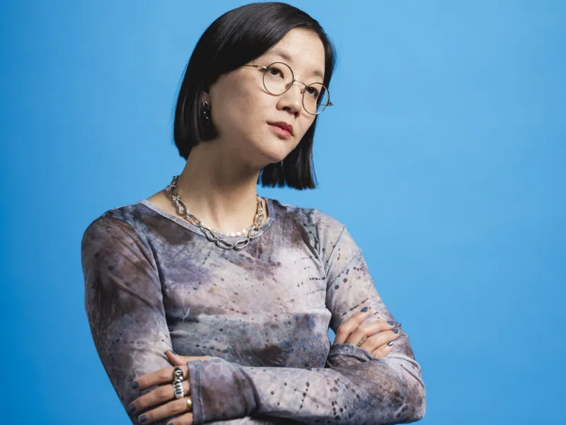 Porträt der Künstlerin Christine Sun Kim mit verschränkten Armen vor einem marineblauen Hintergrund.