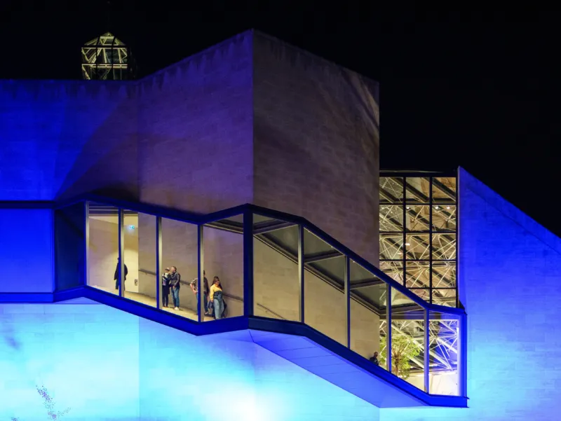A photo of the side of the Mudam Luxembourg building at night, illuminated with blue light.