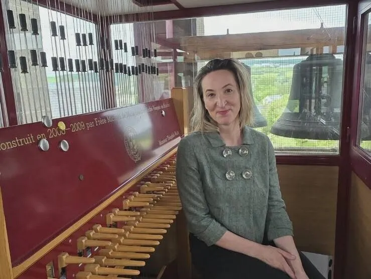 Person sitting beside a carillon, with bells visible in the background.