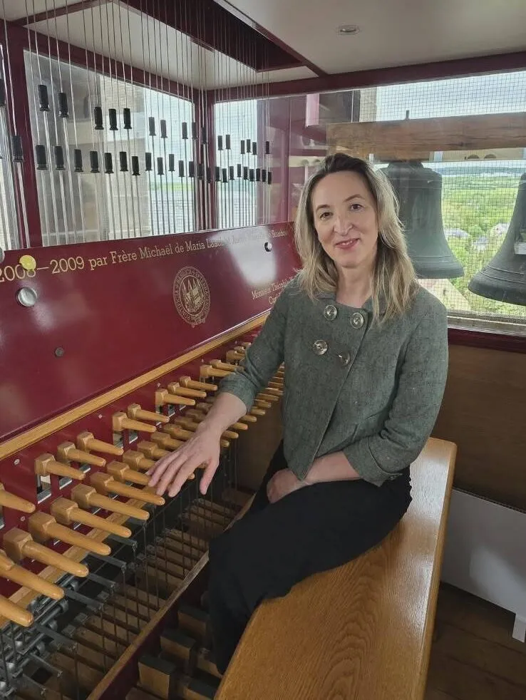 A person sitting next to a carillon, with bells visible behind them.