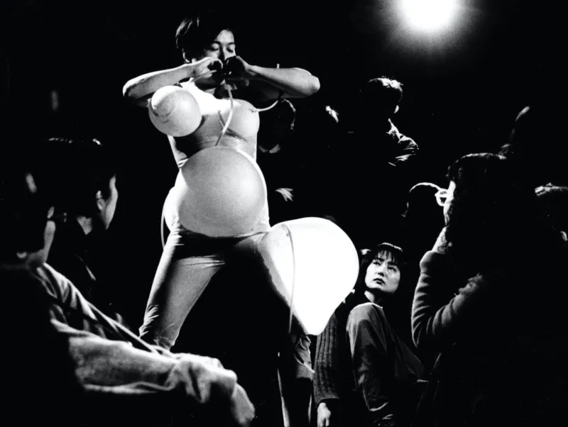 Photo of a performance in Japan showing a person wearing an inflatable costume representing a feminine silhouette.