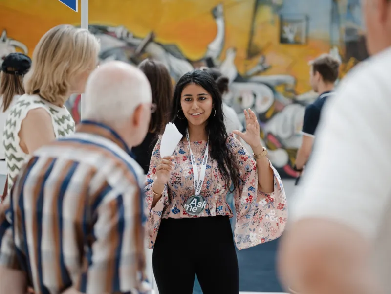 Une jeune femme d’origine non luxembourgeoise explique une œuvre d’art aux visiteurs et visiteuses du Mudam.