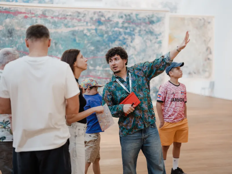 A young man of non-Luxembourgish origin explains an artwork to visitors at Mudam.