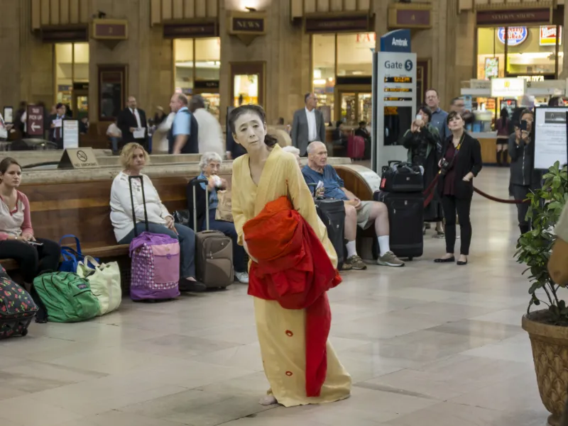 Eine Frau in einem traditionellen Kabuki-Kostüm steht in einer Bahnhofshalle.