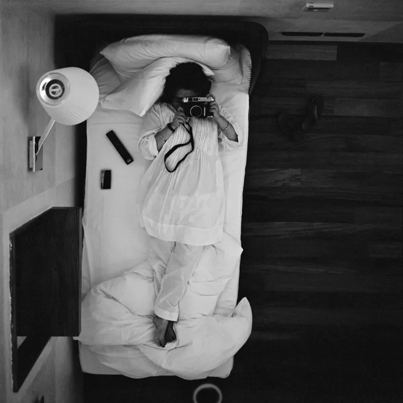 A woman lying on a bed taking a photo.