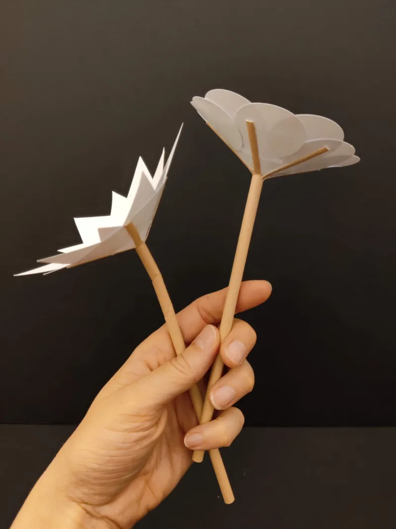 Une main tenant deux fleurs en papier réalisées au workshop de Steve Jakobs.