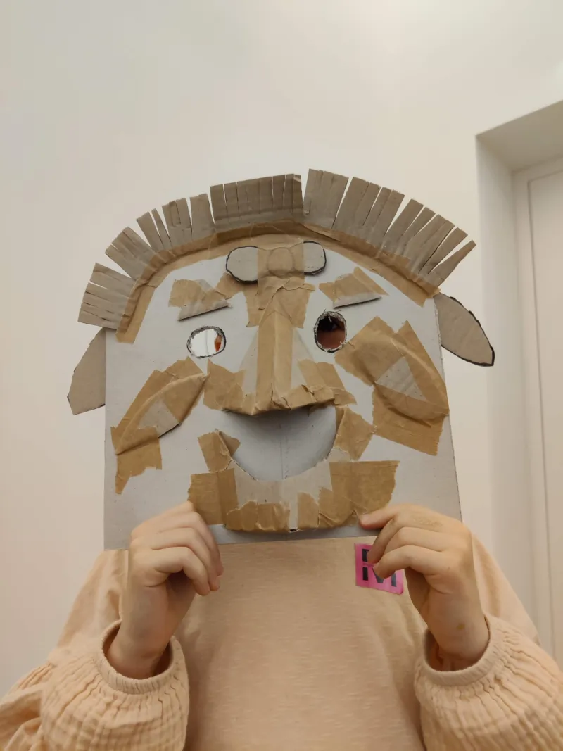 A child holding a cardboard self-made mask in front of his face.