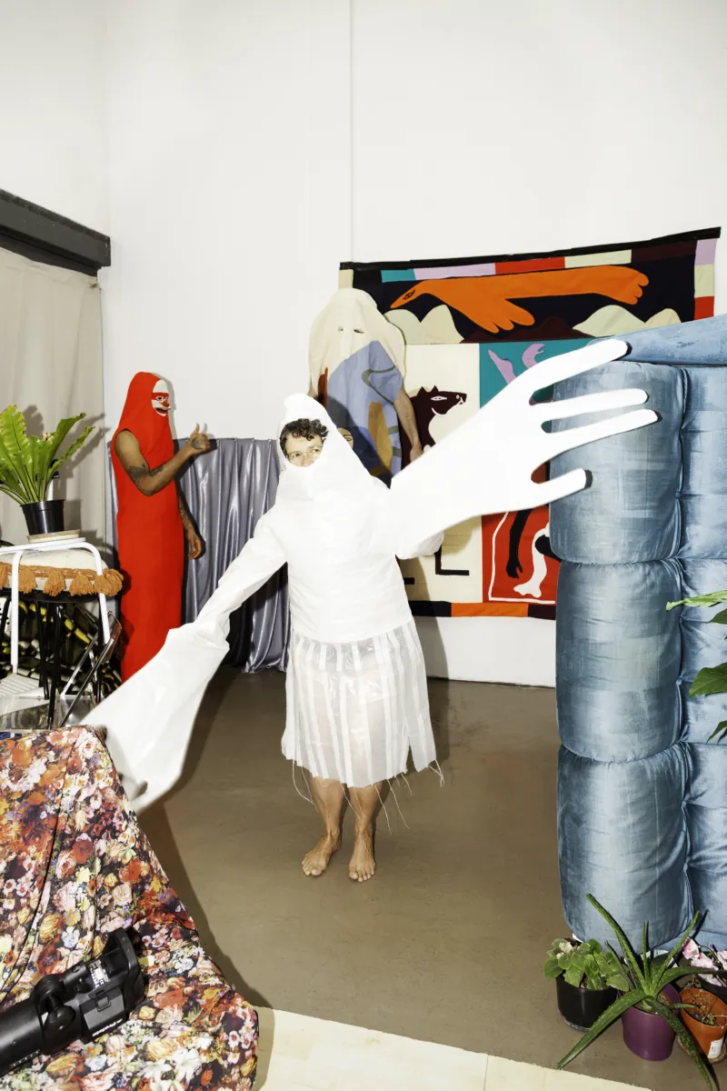 Figure in a white costume with huge hands in front of another figure in a red costume.