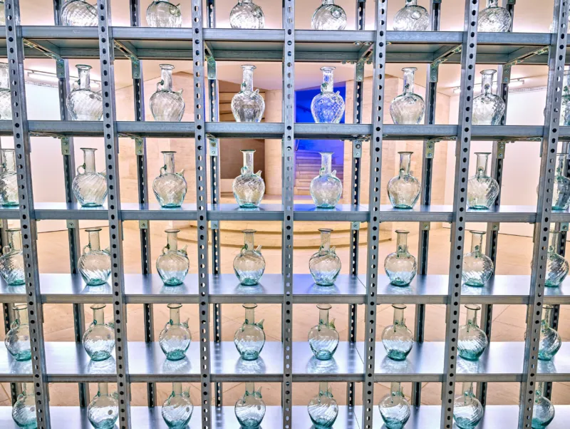 Rayyane Tabet, ‘From Window to Jug’, 2020-2023. 200 cruches en verre recyclé provenant de l’explosion du port de Beyrouth en 2020, unité de stockage construite sur mesure. 300 x 700 cm. Collection Mudam Luxembourg. Acquisition 2024. Vue de l’exposition ‘A Model: Prelude − Rayyane Tabet. Trilogy’, 01.12.2023 – 12.05.2024, Mudam Luxembourg. Photo : Studio Rémi Villaggi © Mudam Luxembourg
