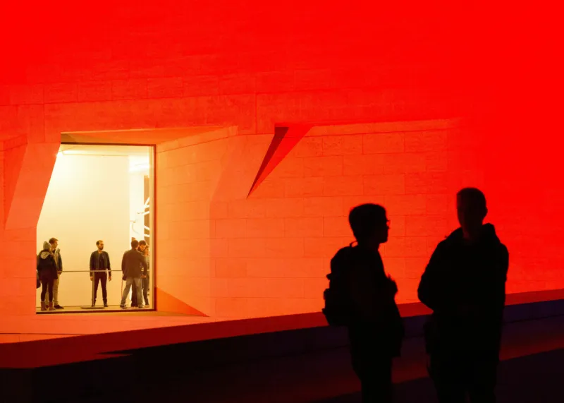 People talking in front of a red-lighted Mudam.