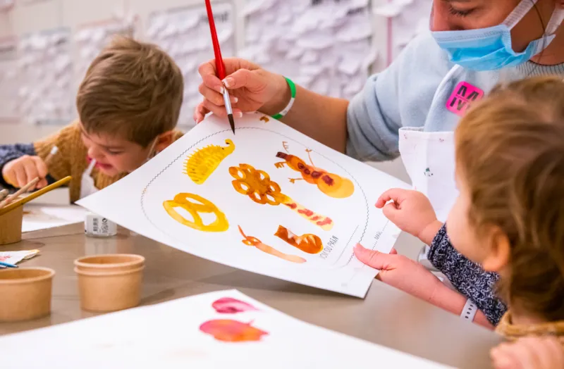 An adult showing two children a drawing of breads from different sizes and shapes.