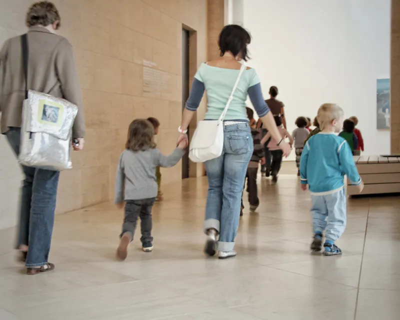 A woman visiting the Mudam museum with two children she is holding by the hands.