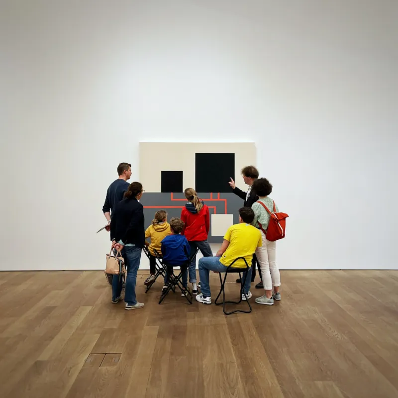 A family gathered around a painting, listening to the explanations of a guide.