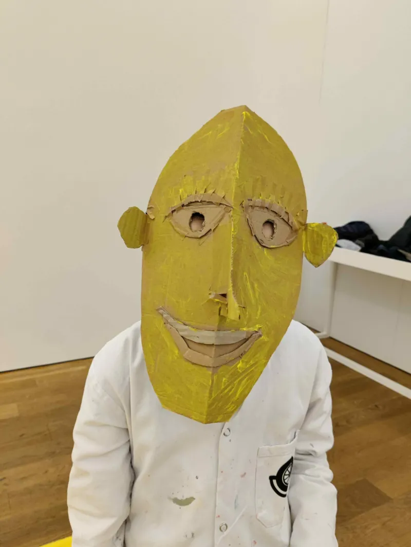 A kid wearing a yellow mask made in a workshop at Mudam.