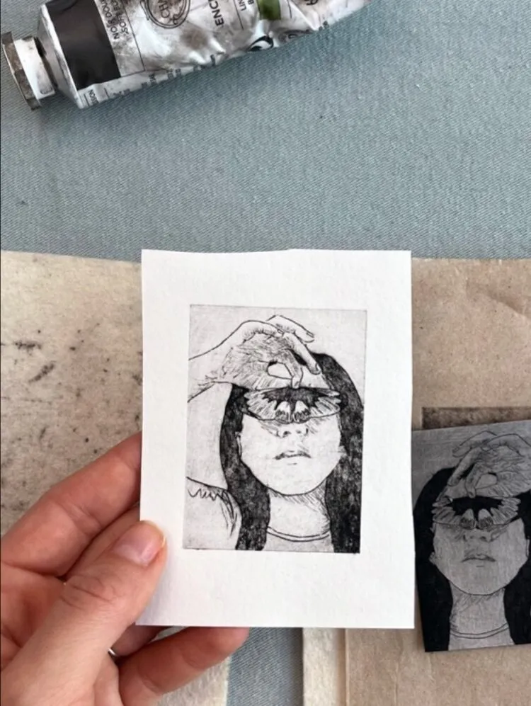 A small kirchen gravure print by Léa Marchet representing a girl's face.