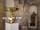 Eine Installation im Inneren einer historischen Kirche. Ein automatisiertes Miniaturkarussell aus weißen Lichtern steht neben einer religiösen Figur.